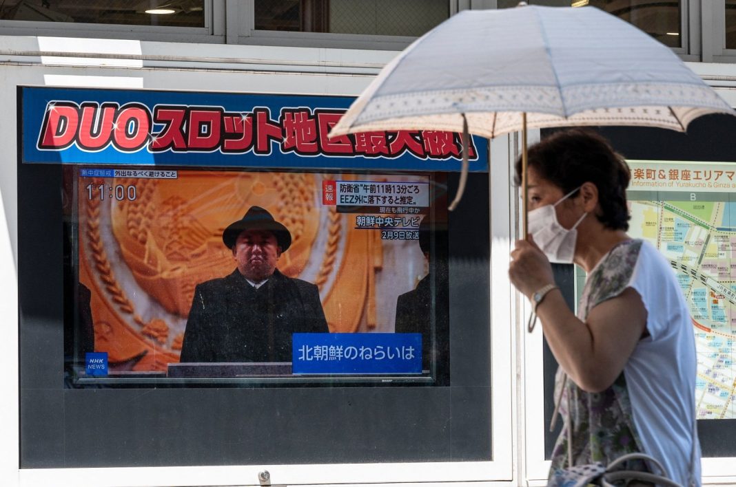 Seorang wanita berlindung dari matahari saat dia berjalan melewati laporan berita televisi tentang peluncuran rudal Korea Utara yang mendarat di luar zona ekonomi eksklusif Jepang di barat negara itu, di sepanjang jalan pejalan kaki di pusat kota Tokyo pada 12 Juli 2023. (AFP File Foto)