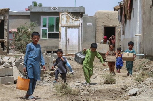Anak-anak Afghanistan membawa barang-barang mereka setelah banjir bandang di daerah Khair Abad di provinsi Ghazni, Afghanistan, 23 Juli 2023. (Foto: AFP)