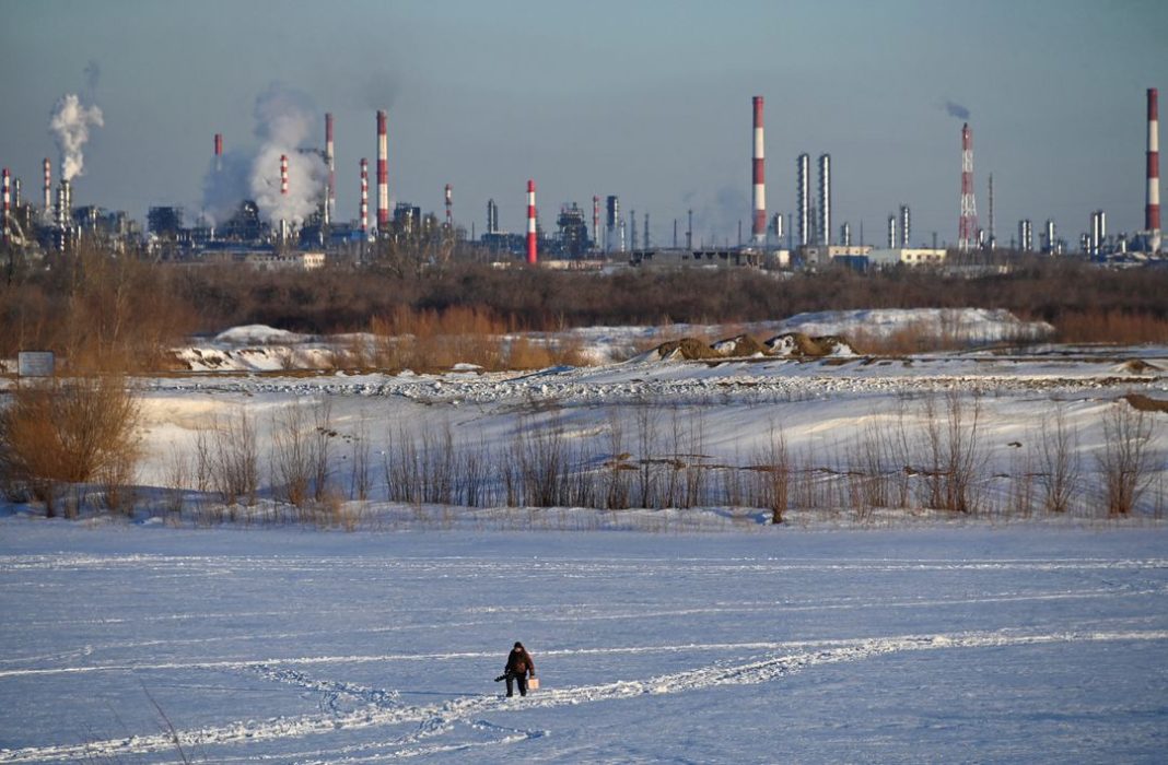 Seorang nelayan berjalan di Sungai Irtysh yang tertutup es di dekat kilang minyak dan pembangkit listrik termal di kota Siberia, Omsk, Rusia, 12 Maret 2023. REUTERS