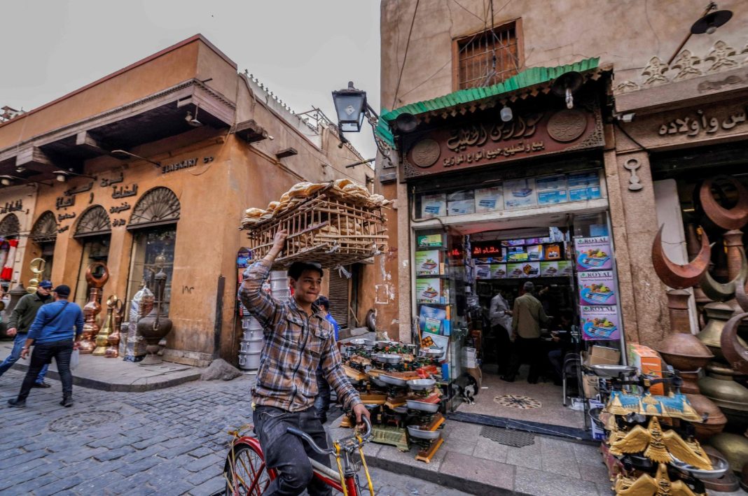 Seorang pengantar menyeimbangkan beban roti di kepalanya saat dia mengendarai sepeda melalui jalan di kawasan tua Kairo, Mesir, 27 Februari 2023. (AFP Photo)